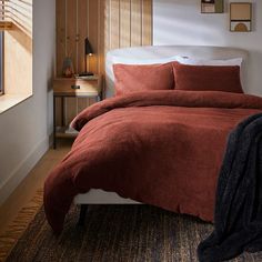 the bed is made up with red linens and brown pillows, along with pictures on the wall