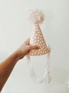 a hand holding a paper party hat with white polka dots on it and a pink ribbon around the top