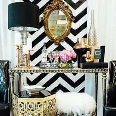 a black and white striped wall with gold accents in a living room area that has two chairs, a table with a mirror on it