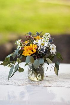 a vase filled with lots of flowers on top of a white table covered in greenery