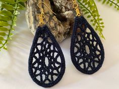 a pair of crocheted earrings sitting on top of a rock next to a plant