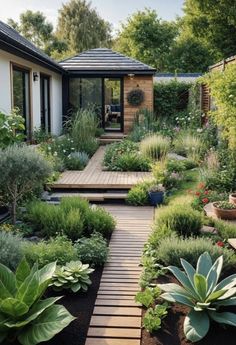 a garden with lots of plants and flowers in the front, along with a wooden walkway