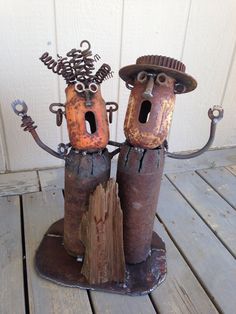 two rusted metal figures with hats and arms holding wrenches on top of each other