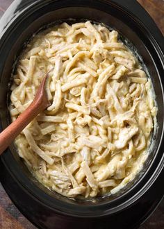 a wooden spoon in a black crock pot filled with macaroni and cheese