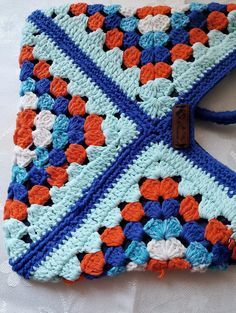 a blue and orange crocheted bag with brown leather tag on it's side