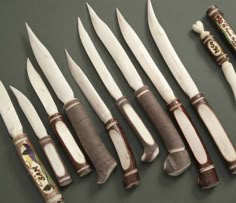 seven knives are lined up next to each other on a gray surface with white handles