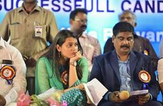 some people are sitting down and one is looking at something in front of them with an award on her hand