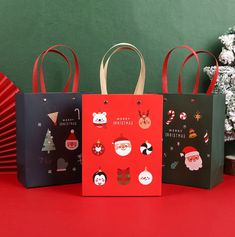 three christmas shopping bags sitting next to each other on a red table with green background