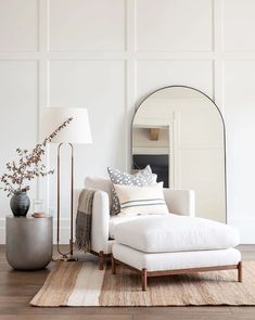 a living room with white walls and wood flooring, a large mirror on the wall