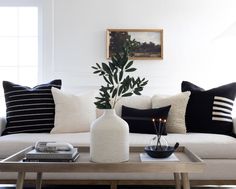 a living room with white couches and black pillows on the coffee table in front of it