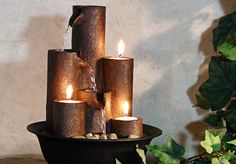 a fountain with lit candles in it sitting on top of a table next to a potted plant