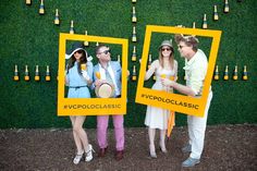 three people standing in front of a green wall holding up yellow frames with photos on them