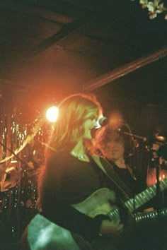 two people on stage playing guitars and singing into microphones with lights in the background