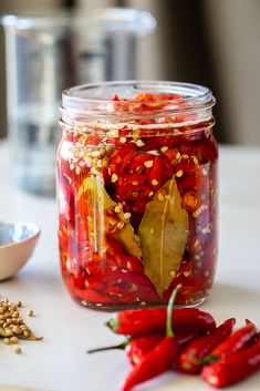 a jar filled with red peppers next to a spoon and pepper flakes on a table