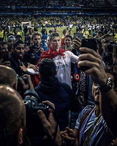 a group of people standing around each other at a soccer game, taking pictures with their cell phones