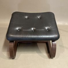 a black foot stool sitting on top of a white floor in front of a wall