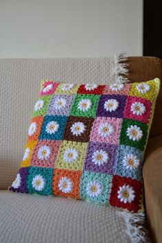 a crocheted pillow with flowers on it sitting on a couch next to a wall