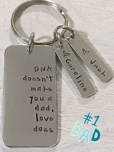 a couple of key chains that are on top of a white surface with the words dna doesn't make you a dad, love, i do