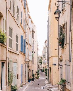 an empty street in the middle of some buildings with shutters on each side and one person walking down it