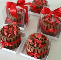 four heart shaped cakes in small boxes with red ribbons and bows on them, sitting on a table