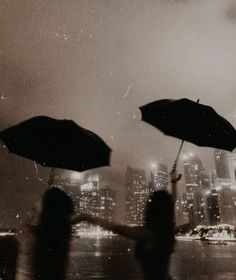 two people holding open umbrellas in front of a cityscape at night time