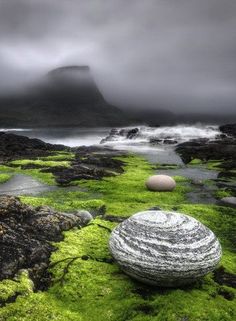 two rocks sitting on top of green moss covered ground next to water and mountains in the background