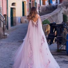 a woman in a pink wedding dress walking down the street with her back to the camera