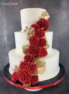 a three tiered white cake with red roses on the side and gold leaf decorations