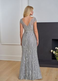 a woman standing in front of a fireplace wearing a silver dress with an open back