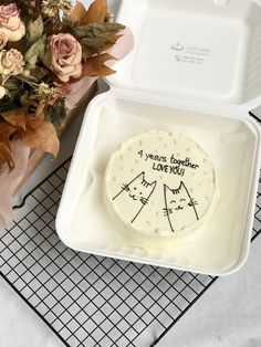 a cake in a white box with writing on it next to flowers and a vase