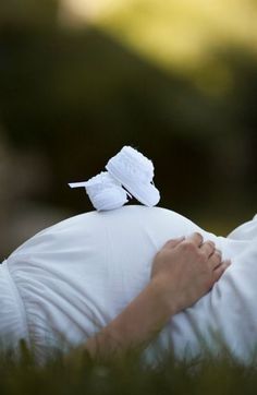 a pregnant woman laying in the grass with her hands on her belly and two white birds perched on top of her head