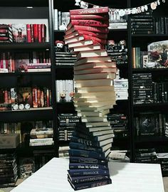 a stack of books sitting on top of a table in front of a book shelf