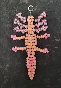 a pink and black beaded cross hanging from a metal hook on a black surface