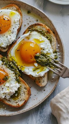 two eggs are on toast with pesto and an egg in the middle is being held by a fork