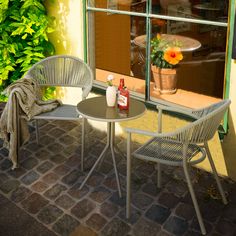 two chairs and a table on a brick patio near a window with flowers in it