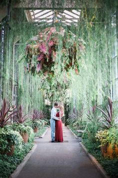 a man and woman are standing in the middle of a walkway surrounded by greenery