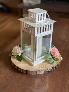 a small white lantern sitting on top of a wooden table next to a pink flower