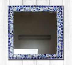 a bathroom mirror with blue and white mosaic tiles on it's sides, hanging on a wall