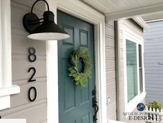 a green wreath on the front door of a house with white trim and black numbers