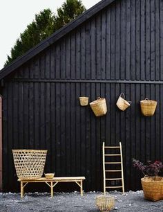 three wicker baskets hanging on the side of a black wall next to two wooden chairs