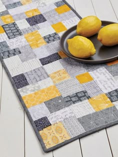 two lemons are on a plate next to some yellow and gray squares that have been made into a patchwork table runner