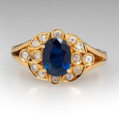 This gorgeous sapphire ring is centered with one (1) oval mixed cut natural sapphire set into a four-prong setting. The sapphire is bordered with fourteen (14), prong/bead set, round brilliant cut diamonds. The ring measures 11.3mm at the top, rises 6.2mm above the finger, tapering to 2.6mm wide and 1.0mm thick at the base of the shank. The ring is currently a size 6.25. Classic Oval Sapphire Ring With Prong Setting, Elegant Oval Cabochon Sapphire Ring, Elegant Yellow Gold Lab-created Sapphire Ring, Classic Oval Sapphire Ring With Rose Cut Diamonds, Gold Sapphire Oval Cluster Ring, Gold Oval Sapphire Cluster Ring, Exquisite Oval Sapphire Ring With Diamond, Oval Sapphire Cluster Ring In Gold, Elegant Sapphire Ring With Oval Cabochon