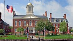 an old brick building with a clock tower and american flags flying in the wind on a sunny day