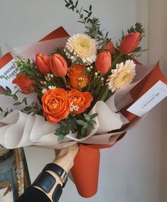 a bouquet of flowers is being held up by someone's hand with an orange ribbon