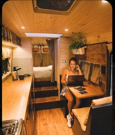 a woman sitting at a table with a laptop in a small room next to a bed