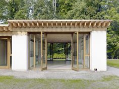 a white building with two open doors in front of it and trees in the background