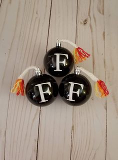 three black glass ornaments with white letters and tassels