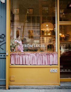 the front window of a flower shop with pink curtains