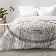 a bed with white sheets and pillows in a room next to a plant on a table