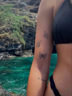 a woman with a butterfly tattoo on her arm next to the ocean and rocks in the background